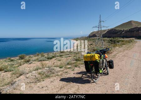 Bici da viaggio con borse si trovano sulla strada vicino al lago Issyk-Kul, paesaggio, Kirghizistan, bicicletta turistica Foto Stock
