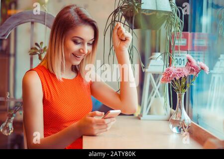 Felice di telefono, vincitore. Donna euforica che guarda il suo cellulare intelligente pompando pugno che celebra guardando felice messaggio foto ha ricevuto sul cellulare a Foto Stock