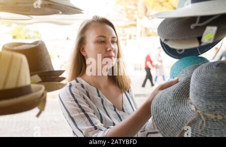 Bella donna che sceglie cappello in negozio in vacanza. Foto Stock