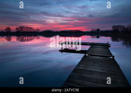 Tramonto con nuvole drammatiche, lago e molo di legno Foto Stock