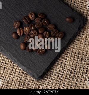 Vista dall'alto del mucchio di chicchi di caffè torrefatto sulla piastra nera sul tessuto del sacco hessian Foto Stock