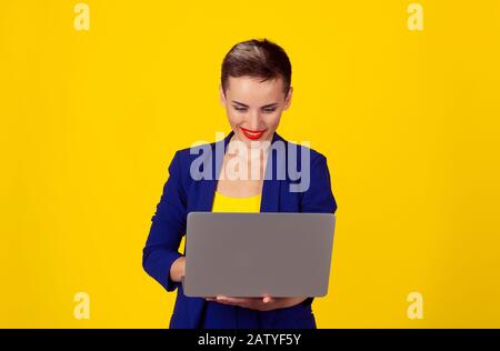 Donna sorridente che invia e-mail sul suo computer portatile isolato sfondo giallo Foto Stock
