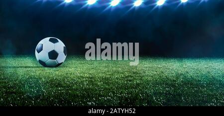 Calcio di fondo o di calcio con una fila di riflettori che illuminano una palla sul tappeto erboso verde in uno stadio in un evento sportivo in una bandiera panoramica Foto Stock