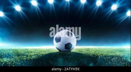 Calcio di fondo o di calcio con una fila di riflettori che illuminano una palla sul tappeto erboso verde in uno stadio in un evento sportivo in una bandiera panoramica Foto Stock