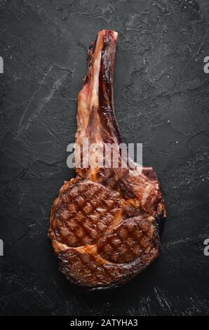 Bistecca di manzo alla griglia, erbe e spezie su sfondo di pietra nera. Barbecue. Vista dall'alto. Spazio libero per il testo. Foto Stock