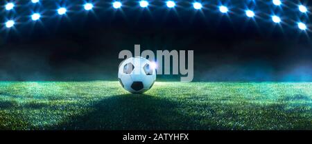 Calcio di fondo o di calcio con una fila di riflettori che illuminano una palla sul tappeto erboso verde in uno stadio in un evento sportivo panorama banner Foto Stock