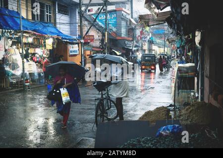 Thiruvananthapuram, Kerala, India - 30 novembre 2017: Persone indiane locali con ombrelloni in una strada commerciale durante la pioggia battente Foto Stock