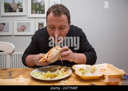 Un uomo seduto a casa con un take-away di un Donner kebab e chip, Regno Unito Foto Stock