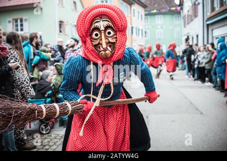 La strega Kandel di Waldkirch, bella strega in blu e rosso lentamente si avvicina e mantiene la scopa in aria. Durante la sfilata di carnevale a Staufen. Foto Stock