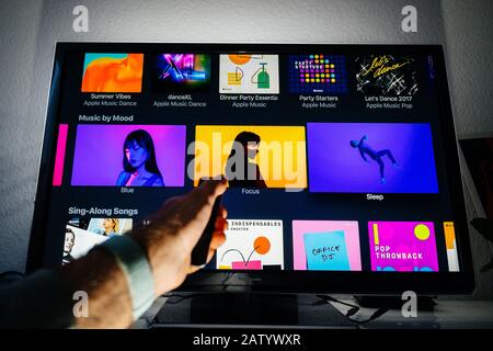 Parigi, Francia - circa 2019: Telecomando manuale per Apple TV di fronte al televisore al plasma Panasonic in soggiorno con musica per playlist personale sui generi Apple Music Blue Focus Sleep Foto Stock