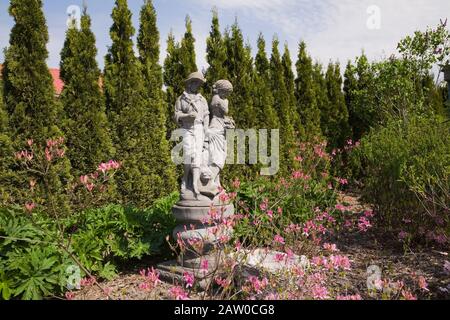 Statua in cemento di un ragazzino e di una ragazza, Azalea - Rododendro 'aurora boreale' delimitata da una fila di Thuja occidentalis 'Maragd' - Cedri alberi Foto Stock