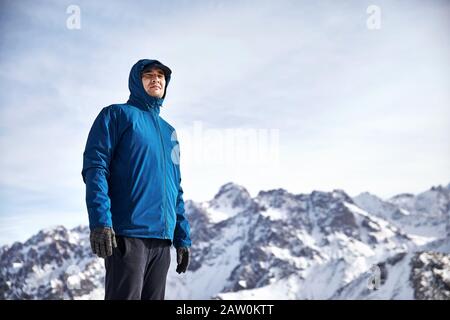 Ritratto di scalatore asiatico in giacca blu su alte montagne innevate sullo sfondo. Arrampicata all'aperto e concetto di alpinismo. Foto Stock