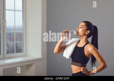 Giovane ragazza bruna beve acqua da una bottiglia dopo l'allenamento in camera Foto Stock