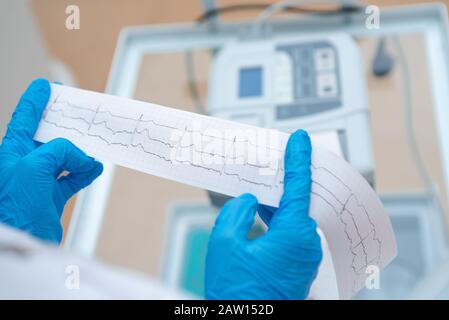 Cardiogramma cardiaco nelle mani di un medico da vicino. Il cardiologo sta studiando la testimonianza di un elettrocardiografo. Foto Stock