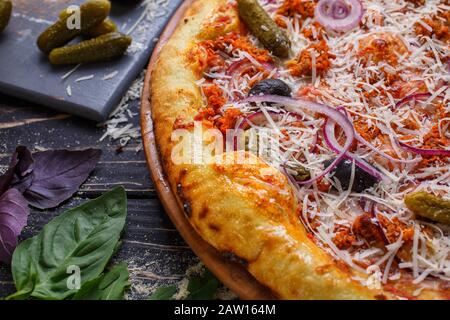 Pizza con formaggio, cetriolo, cipolla, olive al sugo di pomodoro. Pizza italiana. Ingredienti diversi per cucinare la pizza, foglie di rucola Foto Stock