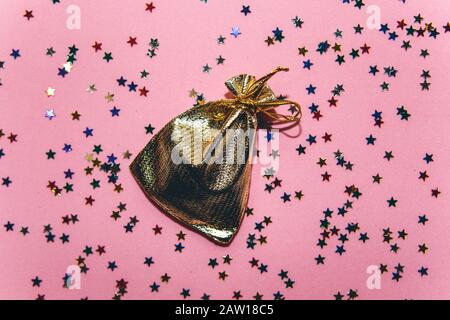 Una piccola borsa regalo dorata su sfondo rosa festoso con tanti confetti a forma di piccole stelle. Foto Stock