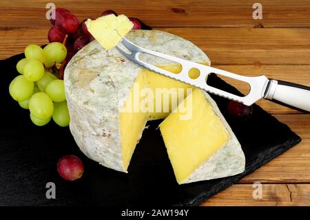 Formaggio cheddar fattoria con un coltello formaggio e taglio cuneo di formaggio su una tavola di ardesia con uno sfondo di legno Foto Stock