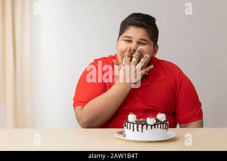 Ragazzo giovane che gli insaccava la bocca con la torta. (Obesità) Foto Stock