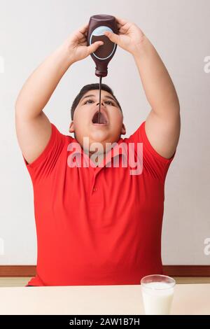 Ragazzo giovane che beve sciroppo di cioccolato direttamente dalla bottiglia. (Obesità) Foto Stock