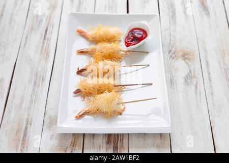 Gamberi croccanti avvolti in pasta Kataifi chiamato anche Kanafeh, Kadaif. Servito con salsa su vecchio sfondo bianco di legno. Foto Stock
