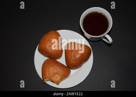 Tre torte su un piatto bianco e una tazza di caffè su uno sfondo nero. Vista ravvicinata dall'alto Foto Stock