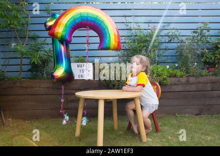 Ragazza di 3 anni seduta ad un tavolo che guarda la stufa in un giardino, Regno Unito Foto Stock