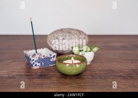 Disposizione di Wellnes. Candela bruciante in vaso di ceramica, bastoncini di incenso, pietra e piante fresche su sfondo di legno. Spiritualità in stile Zen decorazione. Foto Stock