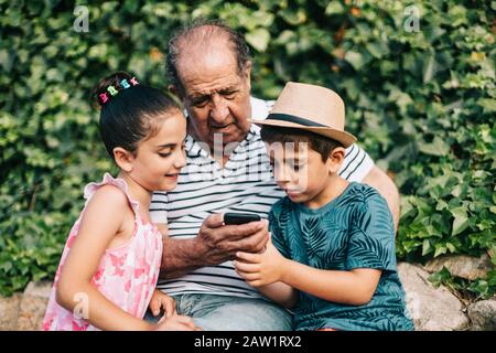 Nonno e nipoti che giocano con un telefono cellulare Foto Stock