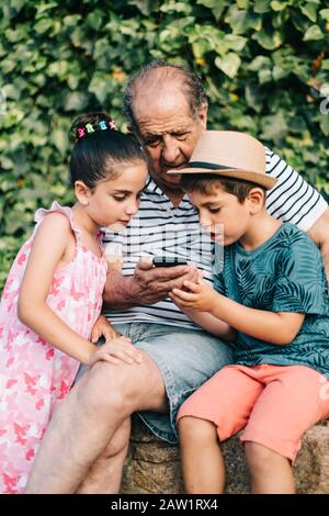 Nonno e nipoti che giocano con un telefono cellulare Foto Stock