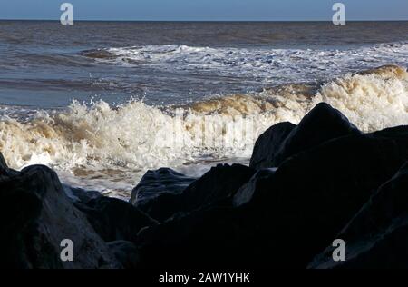 Onde che si infrangono contro una linea di difese importate del mare di roccia sulla costa di Norfolk a Happisburgh, Norfolk, Inghilterra, Regno Unito, Europa. Foto Stock