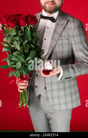 Vista ritagliata dell'uomo in formale indossare fiori e anello di nozze isolato su sfondo rosso. Foto Stock