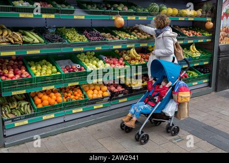 Una sosta madre e bambino per scegliere frutta nutriente e verdura dagli scaffali di arance, banane, mele e uva, fuori da un negozio nel centro di Bromley dove le aziende locali offrono alimenti più freschi e più economici rispetto ai grandi supermercati, il 3rd febbraio 2020, a Londra, Inghilterra. Foto Stock