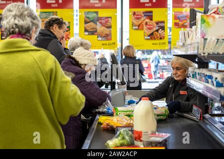 Un cassiere Supermarket che esegue la scansione degli articoli al momento dell'acquisto dal nastro trasportatore e servendo una coda di clienti Foto Stock