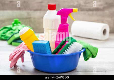 Prodotti per la pulizia sul pavimento, sfondo interno casa. Bottiglie di detergente chimico in un recipiente blu. Pulizia sanitaria domestica o aziendale Foto Stock