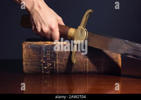 Mano maschio forte con spada e Bibbia Foto Stock