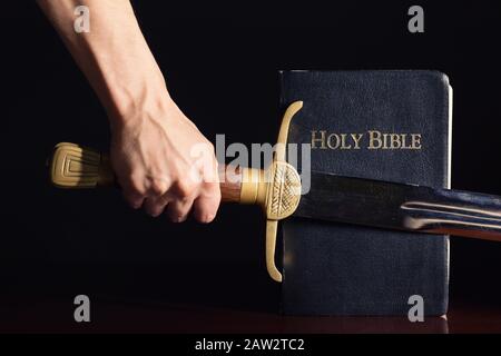 Mano maschio forte con spada e Bibbia Foto Stock