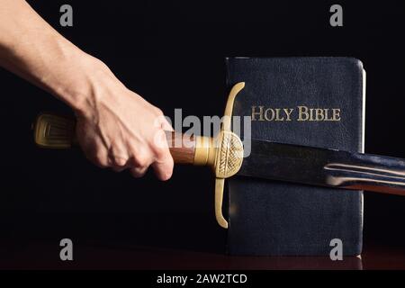 Mano maschio forte con spada e Bibbia Foto Stock