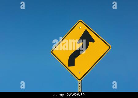 Giallo riflettente strada tortuosa davanti segnaletica stradale isolato su sfondo cielo blu soleggiato Foto Stock