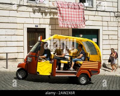 Turisti che viaggiano in un veicolo Tuktuk per visite turistiche a Lisbona, Portogallo Foto Stock