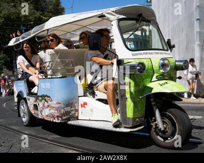 Turisti che viaggiano in un veicolo Tuktuk per visite turistiche a Lisbona, Portogallo Foto Stock