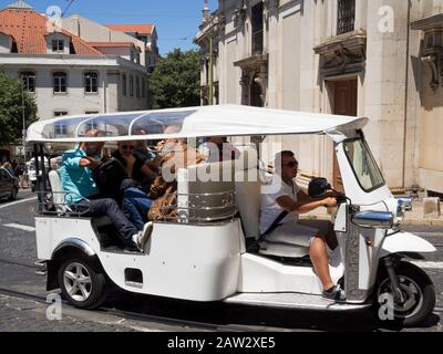 Turisti che viaggiano in un veicolo Tuktuk per visite turistiche a Lisbona, Portogallo Foto Stock