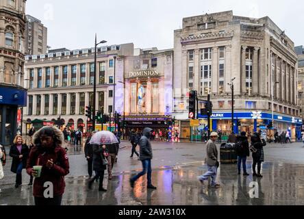 Pendolari e turisti all'incrocio tra Tottenham Court Road e Oxford Street in un pomeriggio invernale piovoso, Londra, Regno Unito Foto Stock