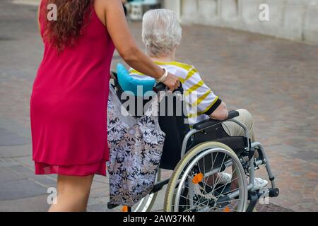 La figlia aiuta la madre anziana in sedia a rotelle Foto Stock