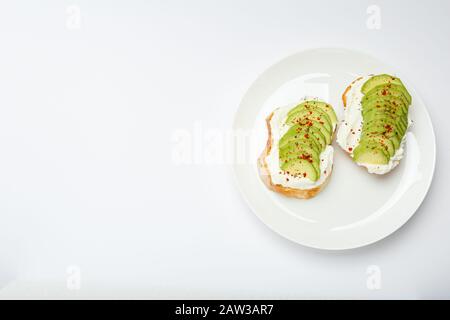 Due toast di avocado, panino di avocado. Avocado fresco affettato su pane tostato di grano, formaggio cremoso. Avocado cosparso di peperoncino, spezie di basilico su un Foto Stock