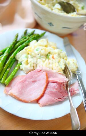Prosciutto, insalata di patate e pasto di asparagi su piatto bianco con coltello e forchetta Foto Stock