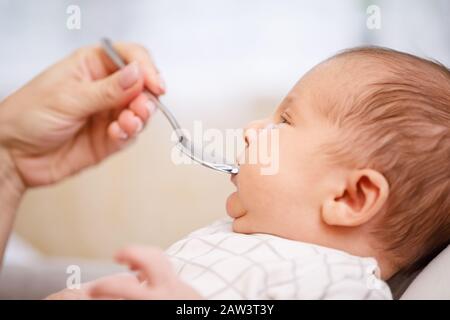 Madre che alimenta il neonato con vitamina o medicinale liquido utilizzando un cucchiaio dosatore Foto Stock