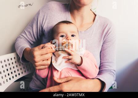 Bambino di 4 mesi rodendo un pollo gamba, degustando i suoi primi alimenti utilizzando il metodo dei led del bambino allo svezzamento BLW. Foto Stock