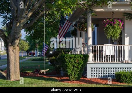 26 luglio 2019 - Città di Clayton, NY, Stati Uniti: Vista laterale delle case su una strada residenziale in estate, altalena albero, American Flags Foto Stock