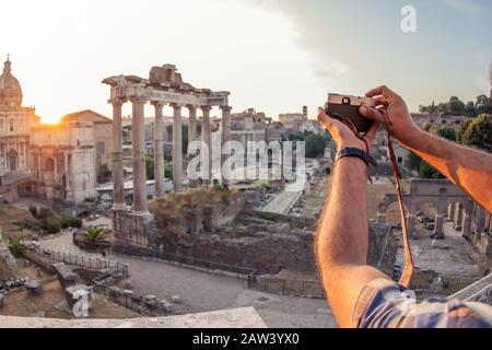 Giovane uomo turista zaino in spalla scattare foto con fotocamera d'epoca al Foro Romano all'alba. Storico Foro Romano imperiale a Roma, Italia da Foto Stock