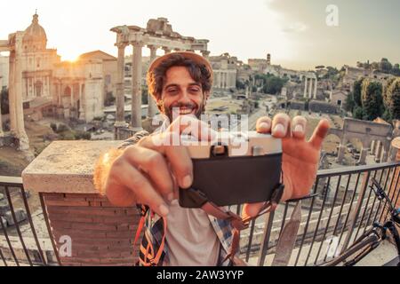 Giovane uomo turistico zaino in spalla che prende selfie con fotocamera d'epoca al Foro Romano all'alba. Storico Foro Romano imperiale a Roma, Italia da Foto Stock